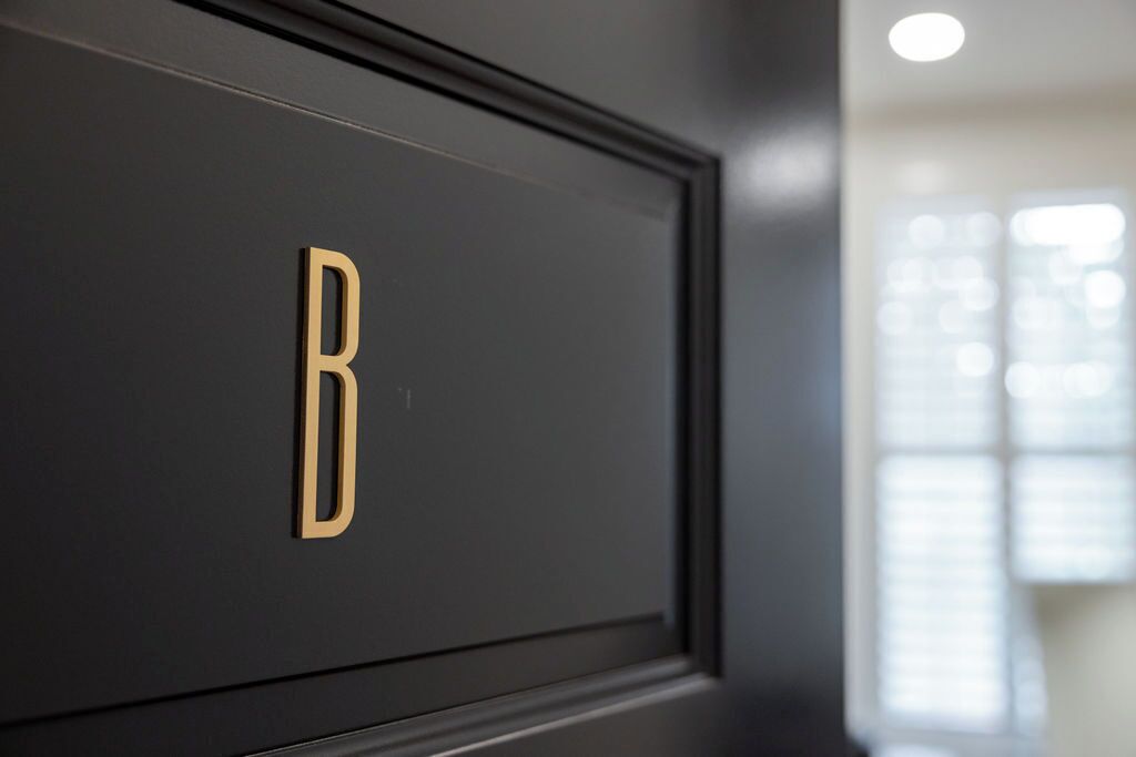 A close-up of a dark-colored door with a gold letter 'B' on it.