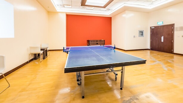 A spacious room with a ping pong table, a projector screen, and a bright orange accent wall. - Sophisticated High-Floor 1BR with Balcony Featuring Partial Sea Views (Dubai)