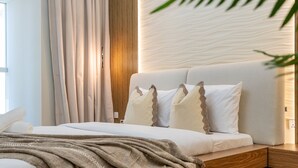 A modern bedroom with a wooden headboard, a bed with white linens, and a textured wall. - Sophisticated High-Floor 1BR with Balcony Featuring Partial Sea Views (Dubai)