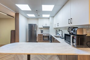 A modern kitchen with a central island, stainless steel appliances, and white cabinetry. - Sophisticated High-Floor 1BR with Balcony Featuring Partial Sea Views (Dubai)