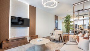 A modern living room with a flat-screen TV, a round coffee table, a sofa, and a chair. - Sophisticated High-Floor 1BR with Balcony Featuring Partial Sea Views (Dubai)