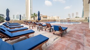 A rooftop pool area with lounge chairs and umbrellas, surrounded by high-rise buildings. - Sophisticated High-Floor 1BR with Balcony Featuring Partial Sea Views (Dubai)