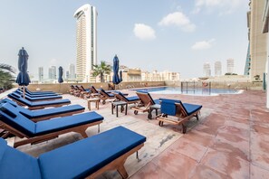 A rooftop pool area with lounge chairs and umbrellas, surrounded by high-rise buildings. - Sophisticated High-Floor 1BR with Balcony Featuring Partial Sea Views (Dubai)