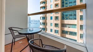 A balcony with a round table and two chairs, overlooking a cityscape with a river and high-rise buildings. - Sophisticated High-Floor 1BR with Balcony Featuring Partial Sea Views (Dubai)