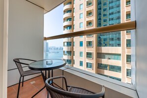 A balcony with a round table and two chairs, overlooking a cityscape with a river and high-rise buildings. - Sophisticated High-Floor 1BR with Balcony Featuring Partial Sea Views (Dubai)