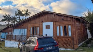 A wooden building with a car parked in front, a hot air balloon in the sky, and palm trees in the background. - Chalé Bello in Pedra Azul (Venda Nova do Imigrante)