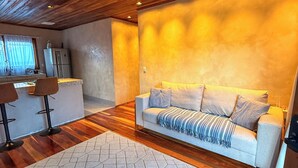 A modern living room with a wooden ceiling, a sofa, a coffee table, and a kitchen area in the background. - Chalé Bello in Pedra Azul (Venda Nova do Imigrante)