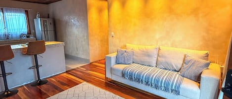 Una sala de estar moderna con techo de madera, un sofá, una mesa de centro y una cocina al fondo.