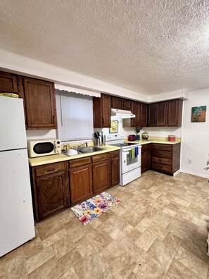 A kitchen with wooden cabinets, a white refrigerator, a stove, and a microwave. - Walk to Downtown & IU • Charming Retreat (Bloomington)