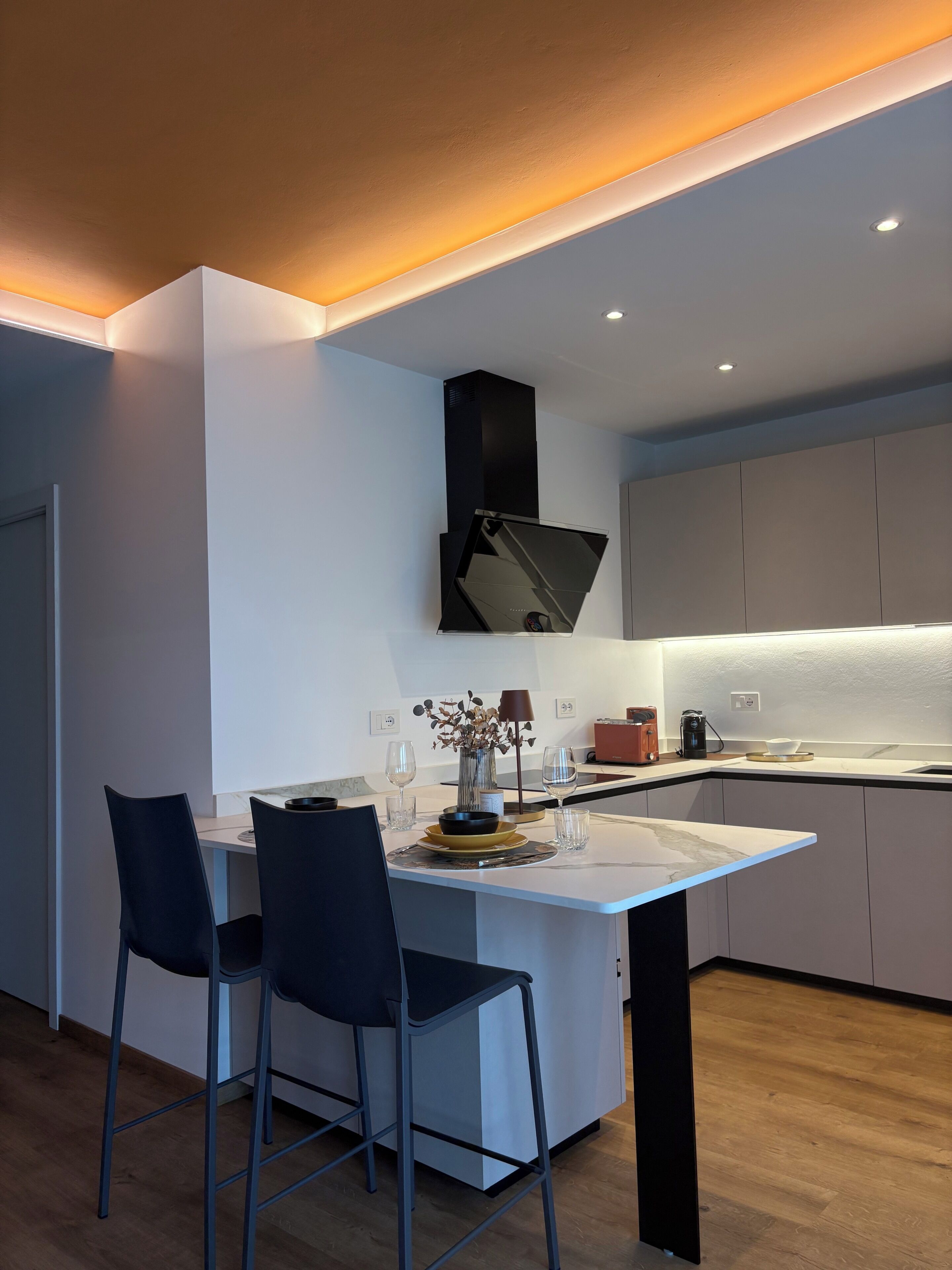 Cocina moderna con una isla central, dos taburetes de bar y una campana extractora empotrada.