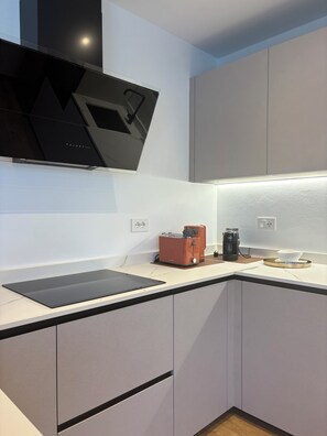 A modern kitchen with a flat-screen TV mounted on the wall, a coffee maker, and a toaster on the counter. - Nido di Rondine Suite Apartments - TRAMONTO (Nago-Torbole)