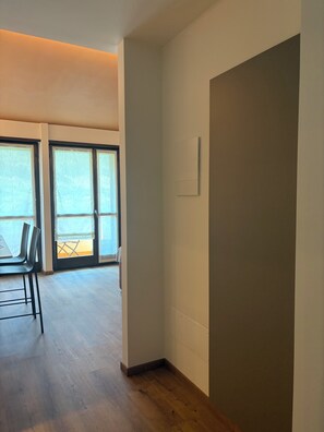 A spacious room with a wooden floor, a dining table with chairs, and a sliding glass door leading to an outdoor area. - Nido di Rondine Suite Apartments - TRAMONTO (Nago-Torbole)