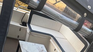 A boat interior with a marble table, cushioned seating, and a window overlooking water.