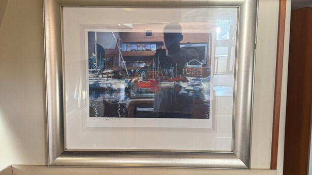 A framed artwork of a marina with boats and buildings, mounted above a blue sofa.