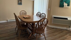 A dining room with a wooden table and chairs, a window with blinds, a wall-mounted air conditioner, and a poster on the wall. - Bigfork Harbor Retreat (Bigfork)