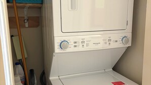 A front-loading white washer and dryer unit with control panel, located in a laundry room with a blue basket on the wall. - Bigfork Harbor Retreat (Bigfork)
