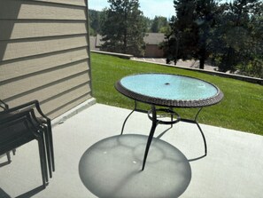 Eine Terrasse mit rundem Tisch und einem Stuhl, eine Rasenfläche und ein Haus im Hintergrund.