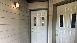 A white door with a decorative metal grille, a doormat, and a wall-mounted light fixture. - Bigfork Harbor Retreat (Bigfork)