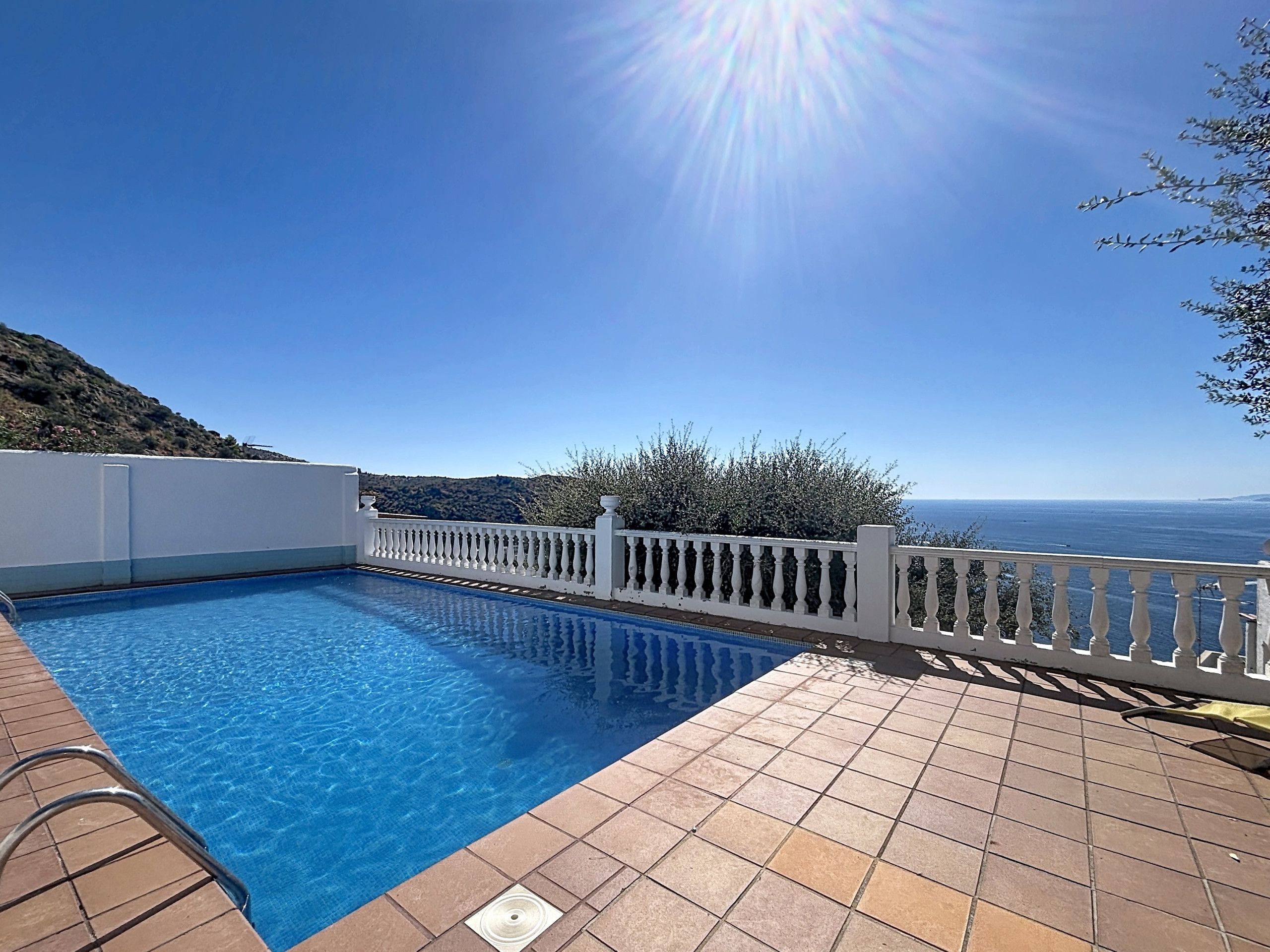 A swimming pool with a white balustrade, clear blue water, and a view of the sea.