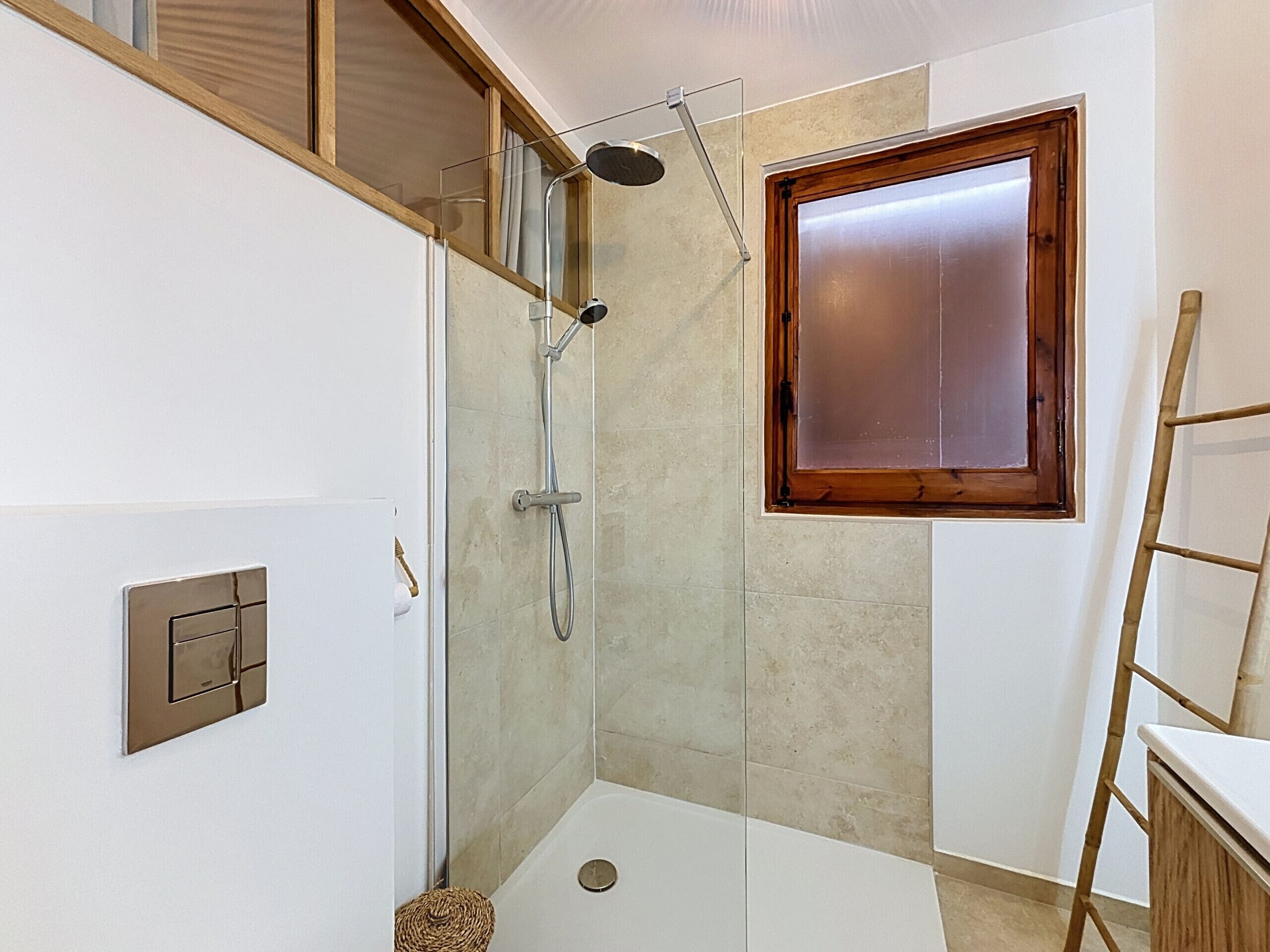 A bathroom with a shower, a window, and a wooden ladder.