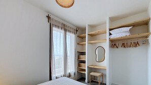 A bedroom with a bed, a wardrobe with shelves, a mirror, and a hanging rack. - BRAMER 36 Rosas / Roses - INTERimmo (Rosas / Roses)
