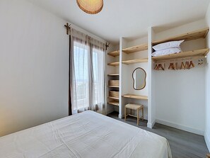 A bedroom with a bed, a wardrobe with shelves, a mirror, and a hanging rack. - BRAMER 36 Rosas / Roses - INTERimmo (Rosas / Roses)