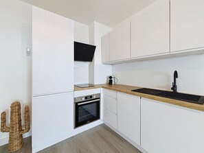 A modern kitchen with white cabinetry, a wooden countertop, a built-in oven, and a black faucet. - BRAMER 36 Rosas / Roses - INTERimmo (Rosas / Roses)