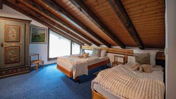 A bedroom with two beds, wooden beams, a dresser, and a painting.