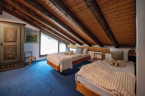 A bedroom with two beds, wooden beams, a dresser, and a painting.