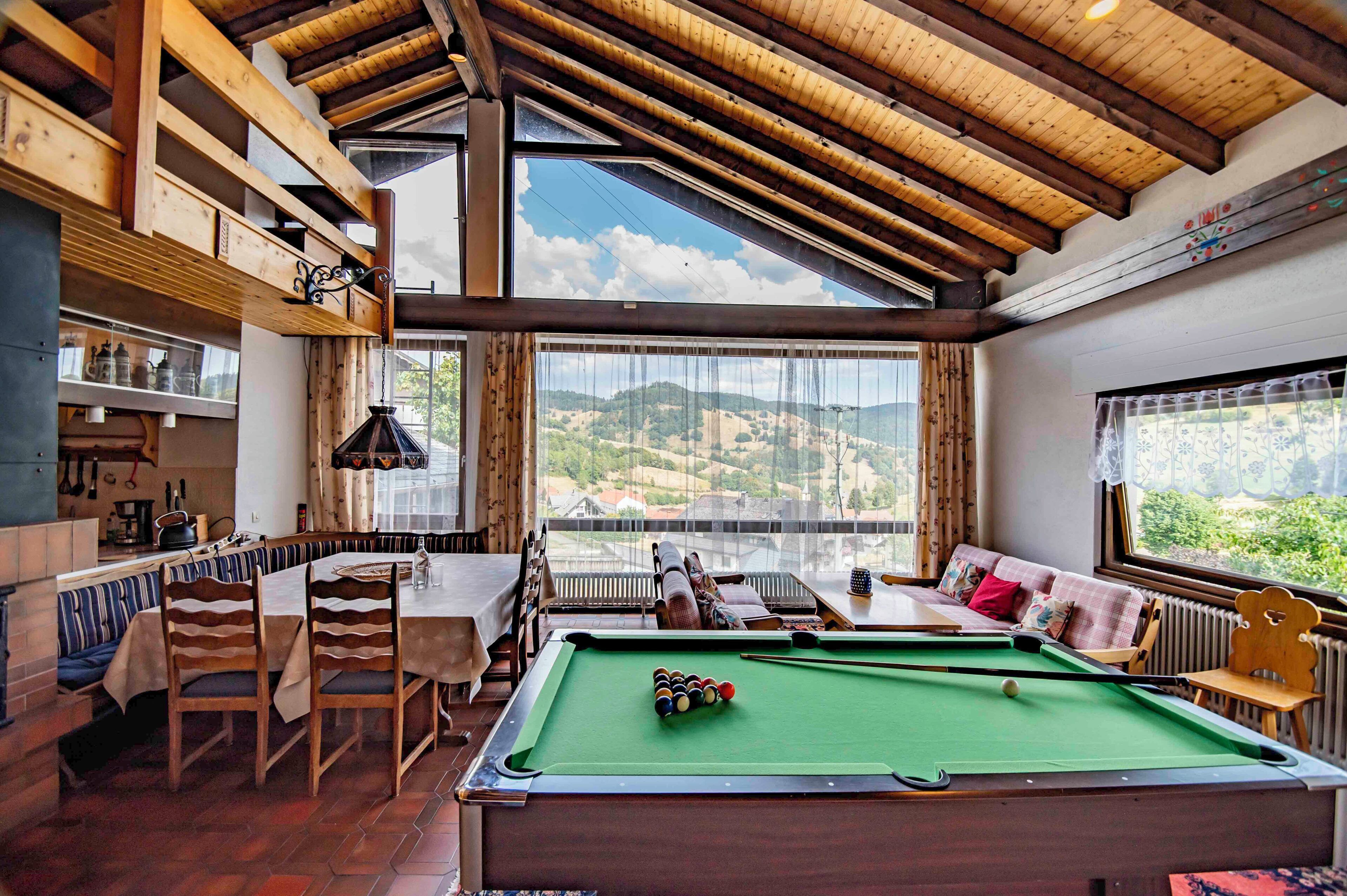 A cozy room with a pool table, seating area, and large windows offering a view of the outdoors.