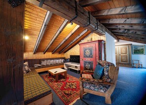 A cozy attic room with wooden beams, a sofa, a cabinet, and a painting on the wall.