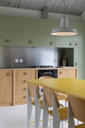 Una cocina moderna con armarios verdes, una campana extractora de acero inoxidable y una mesa de comedor amarilla con sillas de madera.