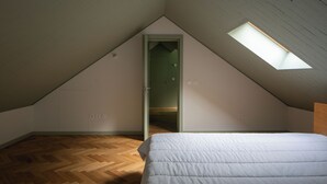 A room with a sloped ceiling, a skylight, a door, and a bed.
