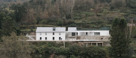 A white building with a flat roof, surrounded by dense vegetation and hills.
