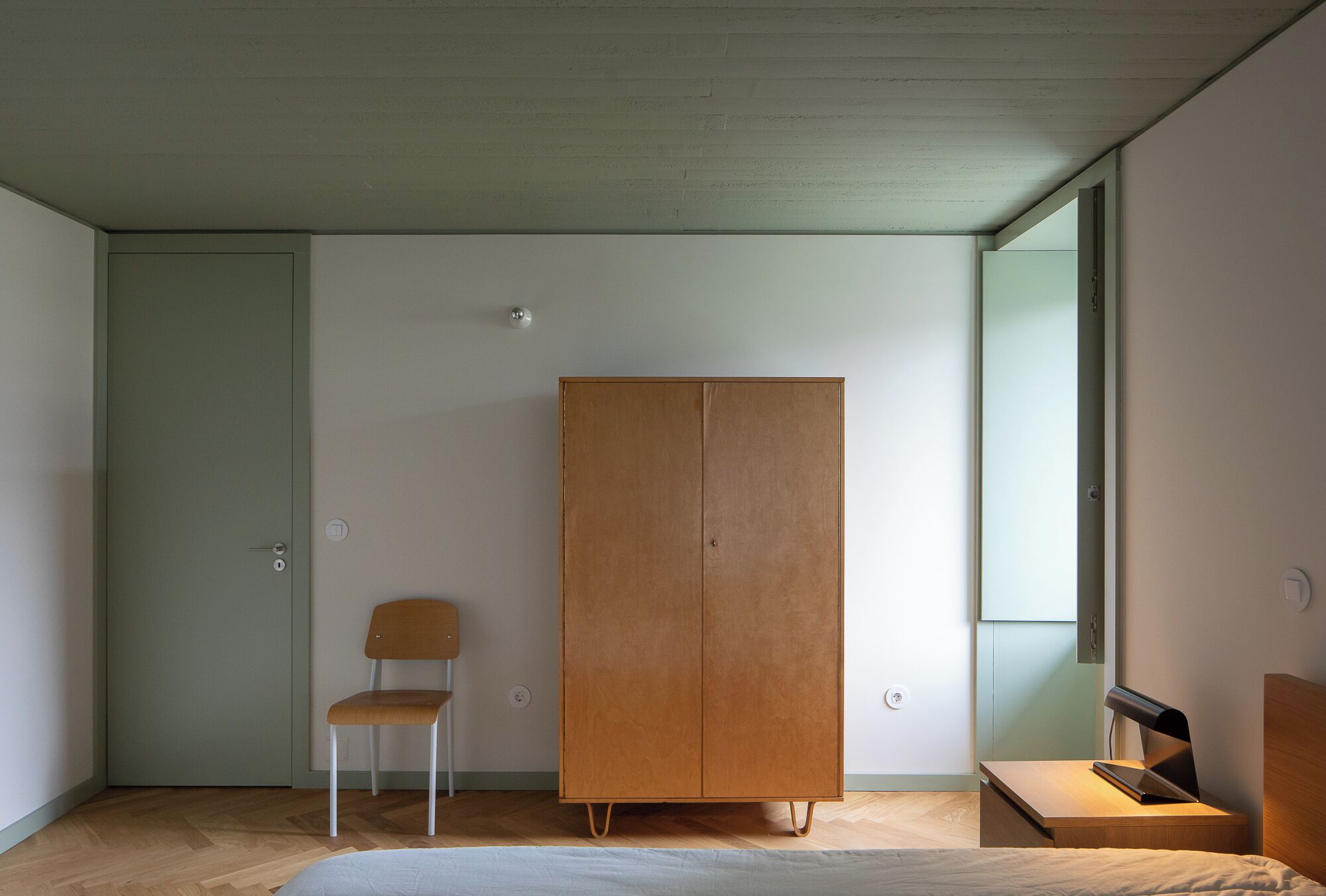Een minimalistisch ingerichte kamer met een houten garderobe, een stoel en een bed.