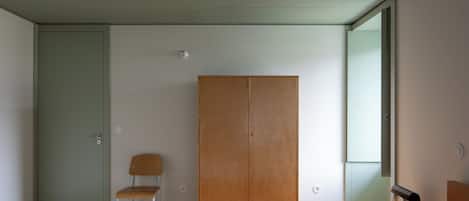 A minimalist room with a wooden wardrobe, a chair, and a bed.
