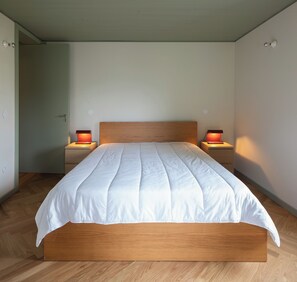 Un dormitorio moderno con estructura de cama de madera, ropa de cama blanca y dos lámparas de noche.