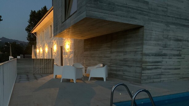 A modern outdoor pool area with a stone wall, two white lounge chairs, and a pool ladder.