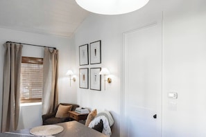Una habitación con una mesa de comedor, dos sillas, un sofá, una lámpara de pared y cuadros enmarcados.