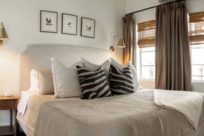 A neatly made bed with a textured blanket, a bedside lamp, and a framed picture of a bird on the wall.