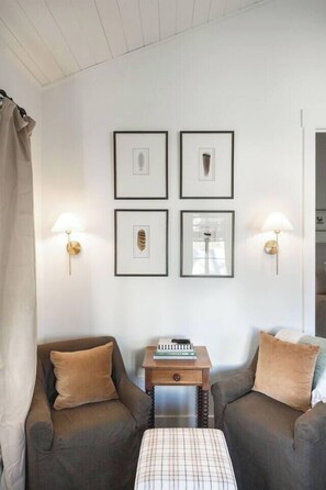 Ein Zimmer mit zwei Sofas, einem kleinen Tisch mit einem Buch und gerahmten Bildern an der Wand.