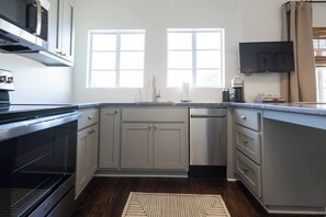 A modern kitchen with grey cabinets, a stainless steel dishwasher, and a flat-screen TV mounted above the counter.