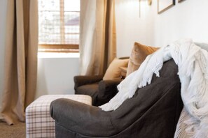 A room with a dark-colored sofa, a white blanket, and a window with curtains.