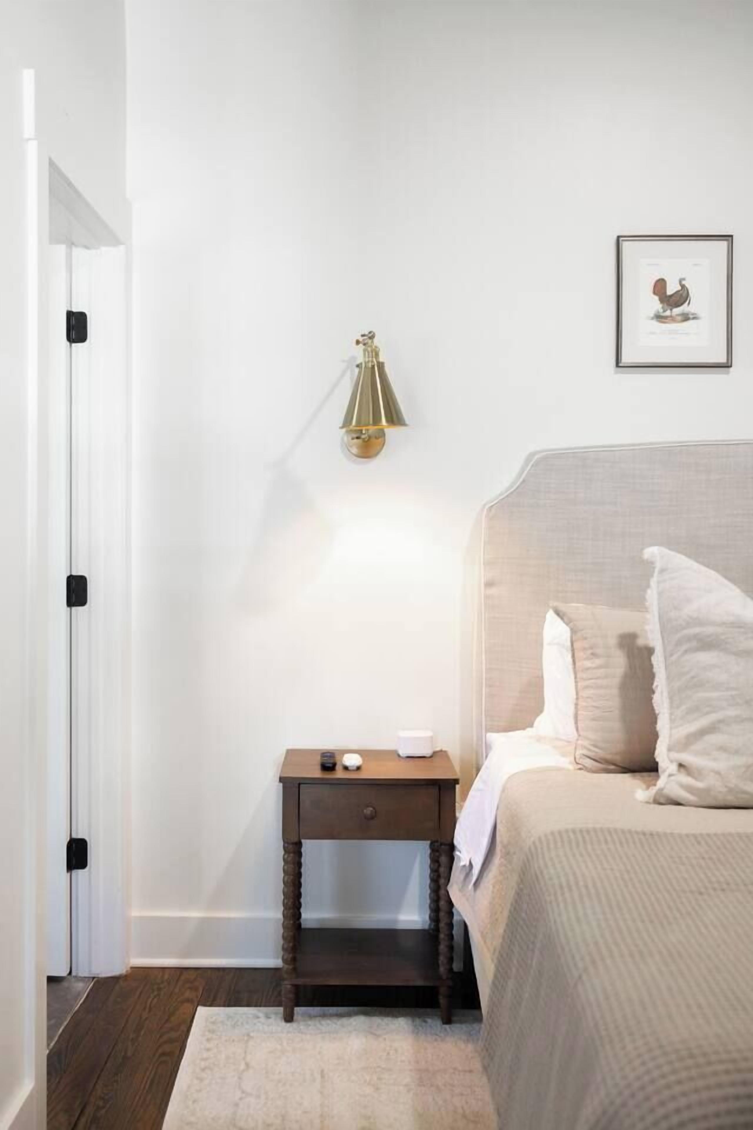 A bedroom with a bed, bedside table, lamp, and a framed picture on the wall.