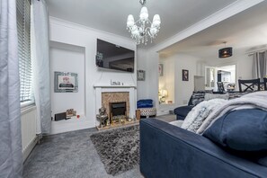 Un salon moderne avec une cheminée, un téléviseur fixé au mur et un lustre.