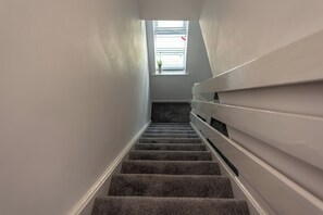 A carpeted staircase with a handrail, leading to a window with blinds. - Charming 3-Bed Home with Private Garden | Sleeps 5 - Pass the Keys (Telford)