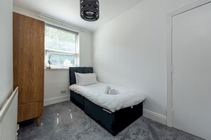 A bedroom with a single bed, a wardrobe, a window with blinds, and a ceiling light fixture. - Charming 3-Bed Home with Private Garden | Sleeps 5 - Pass the Keys (Telford)
