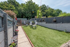 Un jardin avec une pelouse verdoyante, un espace pour s’asseoir à l’extérieur et une clôture en bois.