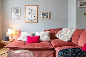 Een woonkamer met een rode bank, een glazen salontafel en drie kunstwerken in lijsten aan de muur.