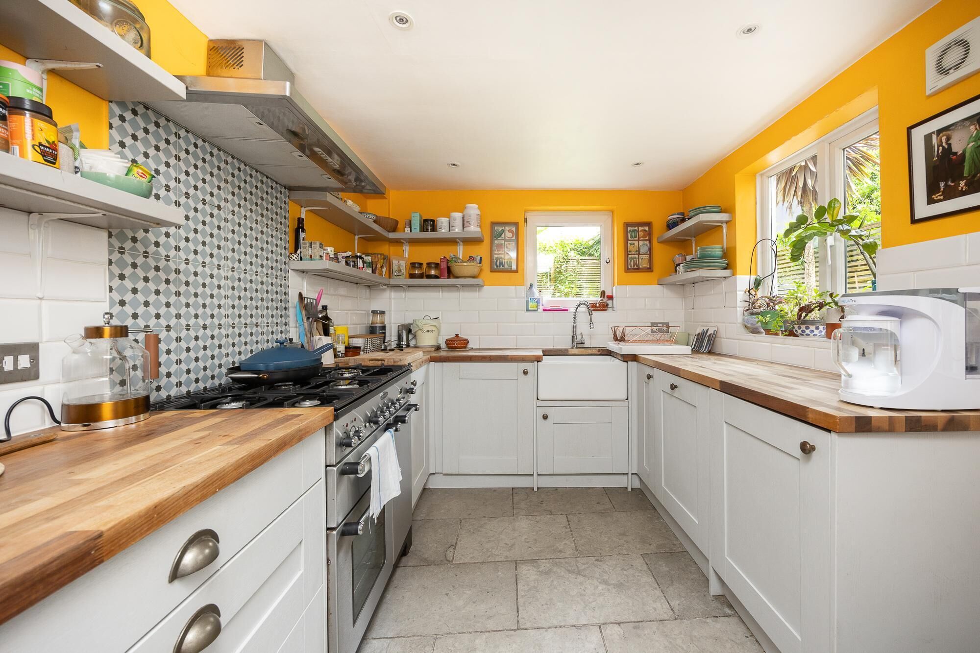 Una cocina con armarios blancos, encimera de madera y ventana con plantas.